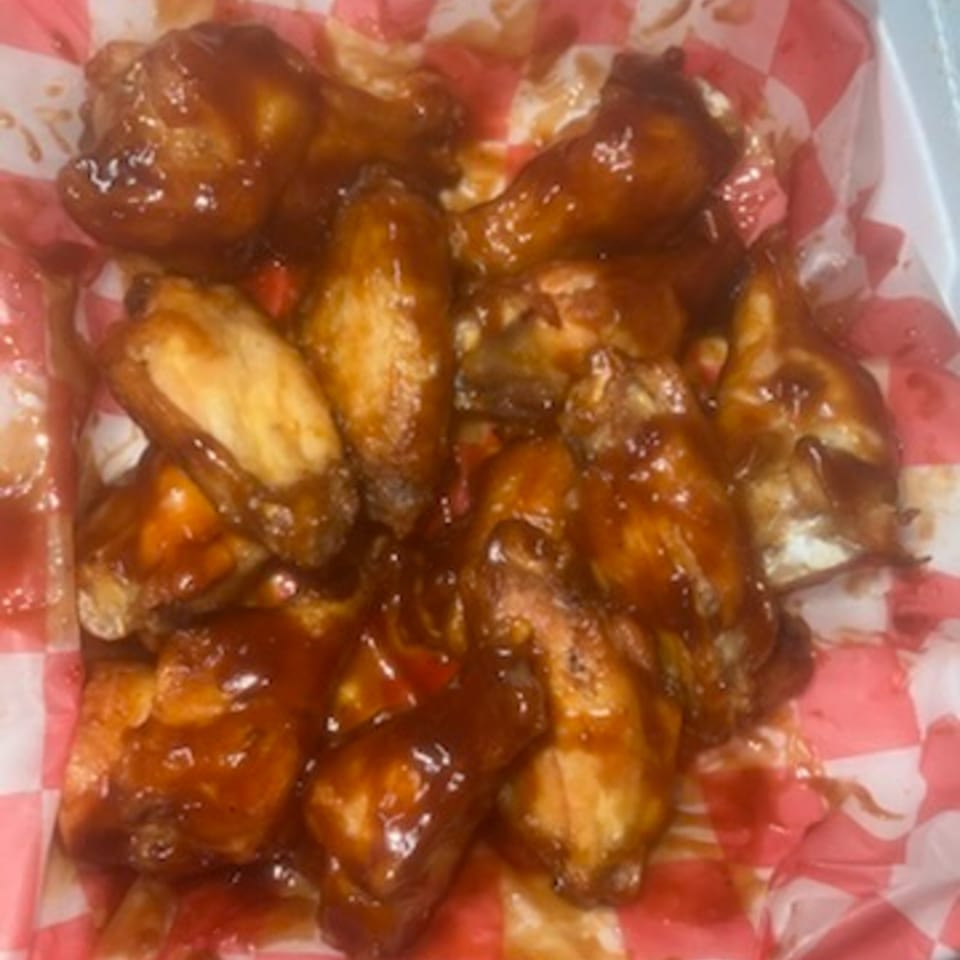 Pappy J's BBQ chicken wings, glistening with sauce, served in a red and white checkered paper-lined basket.