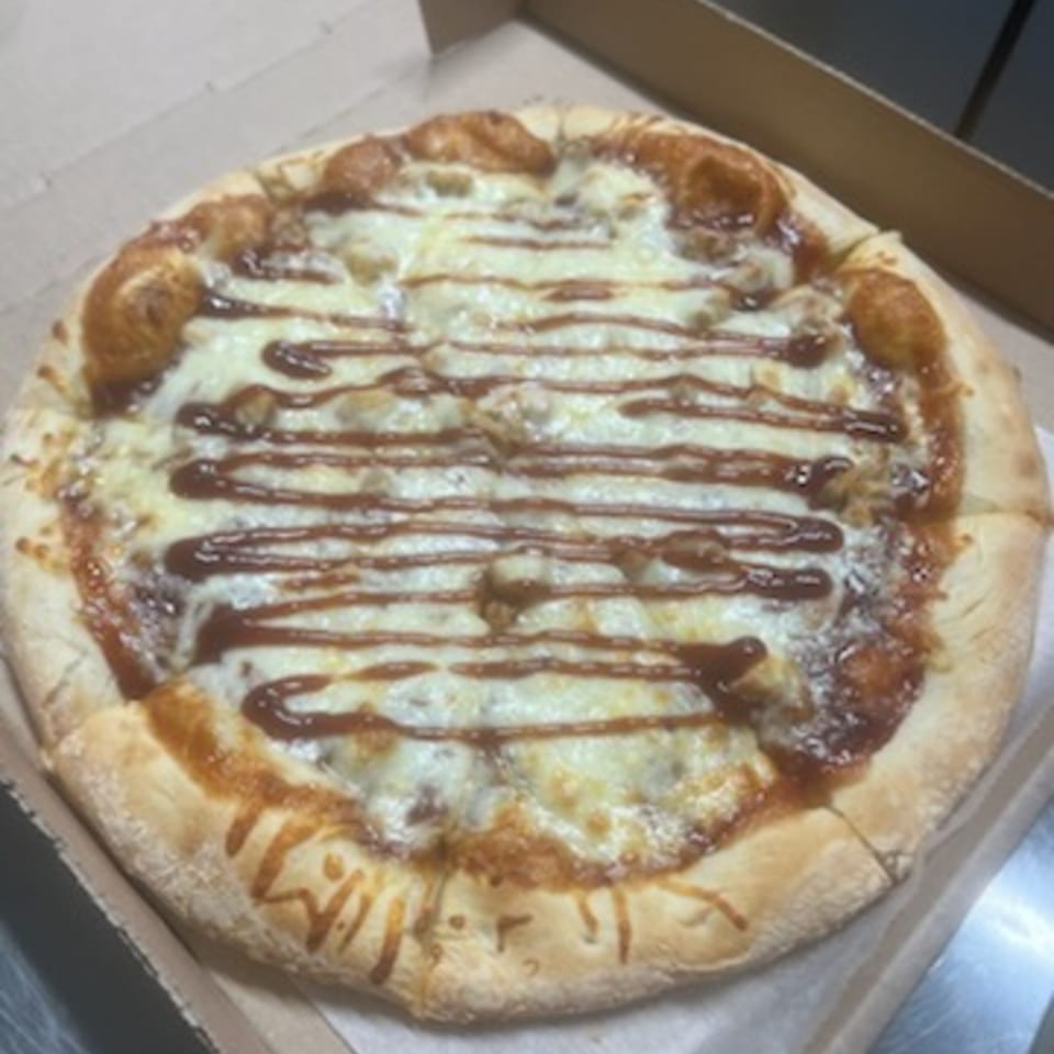 A Pappy J's pizza with melted cheese and a drizzle of BBQ sauce in a cardboard box.